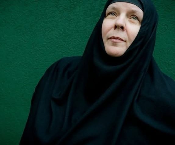 Moniale orthodoxe vêtue de noir, le regard levé, devant un mur vert