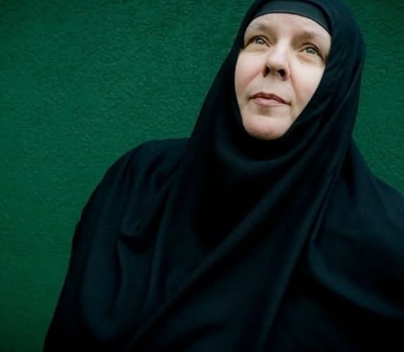 Moniale orthodoxe vêtue de noir, le regard levé, devant un mur vert